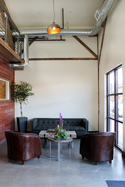 A downstairs seating area featuring leather armchairs, concrete floors, and exposed beams 